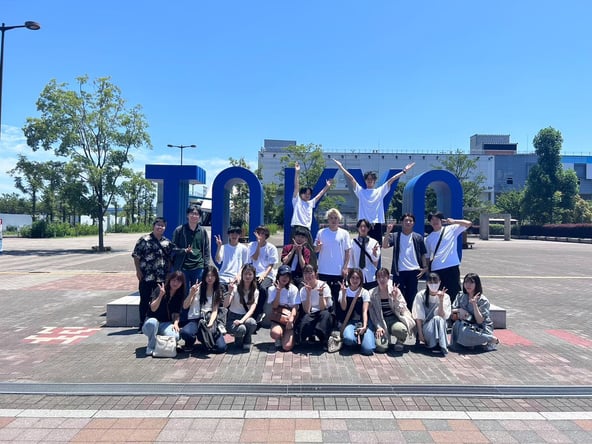 A group posing beside large TOKYO letters outdoors